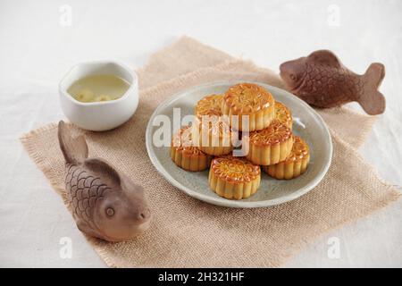 Traditionelle festliche Mondkuchen und eine Tasse Kamillentee werden zum Herbstfest auf einem mit Lehmfischen verzierten Tisch serviert Stockfoto