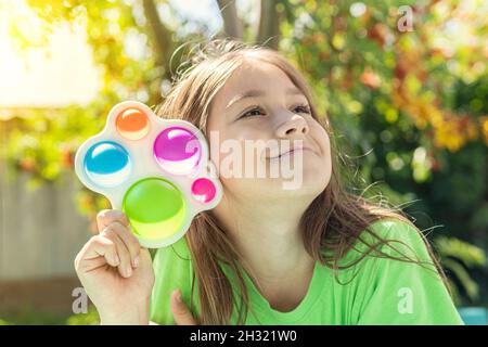 Portrait Mädchen mit modernen einfachen Grübchen Spielzeug. Bunt und hell Pop es Spielzeug einfache Grübchen. Trendy Antistress Sinnesspielzeug Fidget Push Pop it. Lustig gir Stockfoto