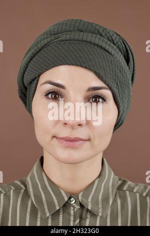 Gesicht einer jungen muslimischen Frau in Kopfbedeckung und gestreiftem Hemd, die vor der Kamera steht und Sie anschaut Stockfoto