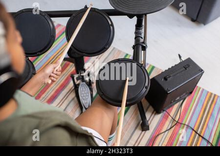 Schulmädchen mit hölzernen Drumsticks, die während der Wiederholung vor dem Drumset sitzen und auf eines der Trommeln schlagen Stockfoto