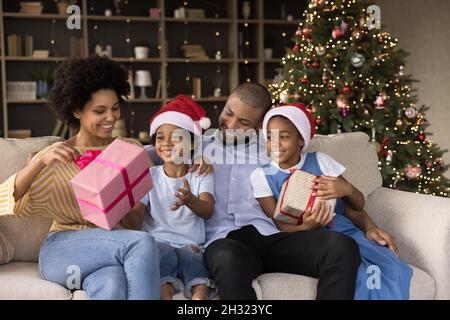 Lächelnde junge afroamerikanische Eltern packen Geschenke mit Kindern aus. Stockfoto