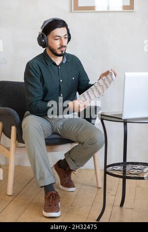 Junge Musiklehrerin mit Kopfhörern, die den Schülern während des Online-Unterrichts Notizen auf dem Laptop-Bildschirm zeigt Stockfoto