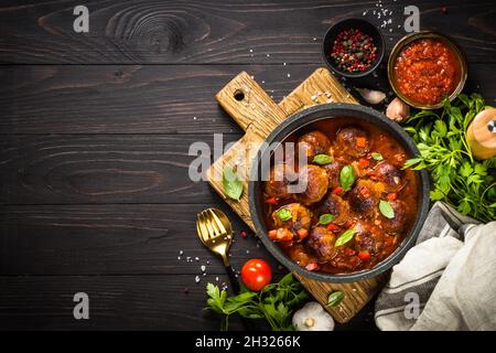Fleischbällchen in Tomatensauce in einer Pfanne auf einem dunklen Holztisch. Stockfoto