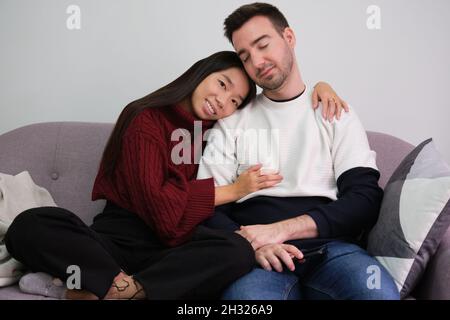 Junges Paar, das sich zu Hause mit einem Laptop auf der Couch entspannt und umarmt. Stockfoto