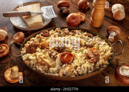 Risotto ai funghi, Pilzrisotto, rustikaler Reis mit Pilzen und Käse, mit Zutaten, auf dunklem Holzboden Stockfoto