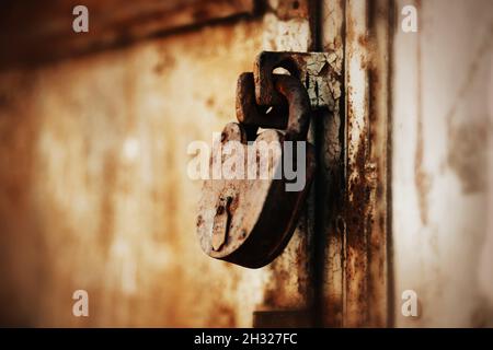 Ein großes altes rostliches Vorhängeschloss schließt das alte zerrissene verlassene Tor. Geschlossen. Geheim. Stockfoto