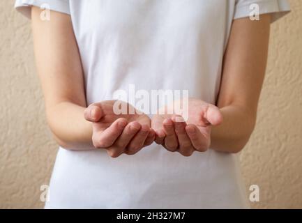 Modell zum Einfügen von Text. Eine Frau in einem weißen T-Shirt, die etwas auf den Handflächen ihrer beiden Hände zeigt, die sich für den Platz der Objektkopie halten. Stockfoto