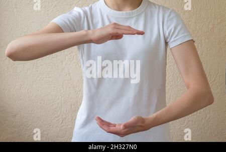 Layout zum Einfügen von Text. Eine Frau in einem weißen T-Shirt, die etwas an den Handflächen ihrer offenen Hände hält. Platz für Objekt kopieren. Stockfoto
