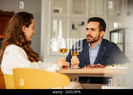 Beschnittenes Porträt eines jungen Paares, das ein romantisches Date hat, Weißwein trinkt und Gespräche genießt Stockfoto