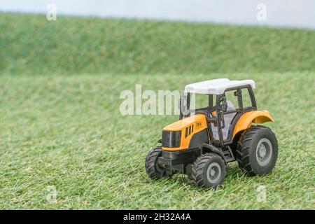 Kleiner Spielzeugtraktor, der auf einem „Feld“ aus faux/fake Gras steht. Für die britische Lebensmittelproduktion, Farm-to-Fork, Field-to-Fork/Field-to-Plate und die britische Landwirtschaft. Stockfoto
