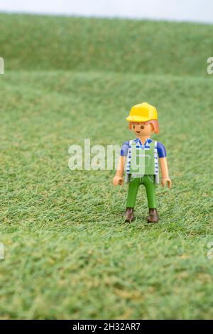 Kleines Spielzeug Playmobil Landwirt Figur steht in "Feld" aus faux / gefälschte Gras. Für die britische Lebensmittelproduktion: Farm to Fork, Field to Fork / Field to Plate. Stockfoto