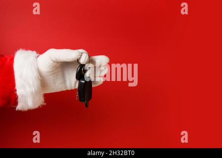 Santa claus hält den Autoschlüssel auf rotem Hintergrund, Kopierraum Stockfoto