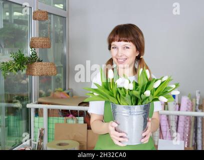 Porträt einer hübschen Floristin mit weißen Tulpen in einem Blumenladen. Business-, Verkaufs- oder Blumendesign-Konzept. Stockfoto