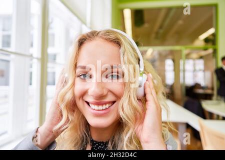 Lächelnde junge Frau, die Kopfhörer trägt, während sie im Büro Musik hört oder Videokonferenzen macht Stockfoto