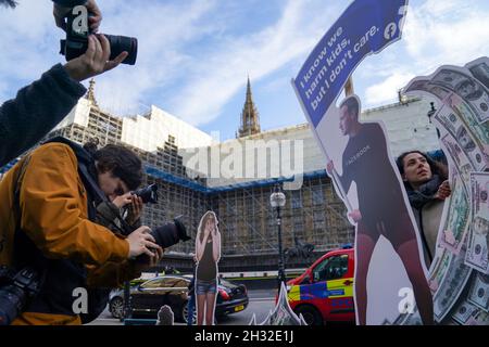 Die hochrangige Aktivistin Flora Rebello Arduini (rechts) mit einer 4 Meter hohen Installation, in der Mark Zuckerberg auf einer Geldwelle surft und von Teenagern umgeben ist, vor den Houses of Parliament in London, bevor Facebook-Whistleblower Frances Haugen die Abgeordneten im Rahmen der Regierungspläne für die Regulierung der sozialen Medien bezeugt. Bilddatum: Montag, 25. Oktober 2021. Stockfoto