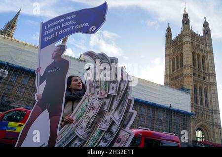 Die hochrangige Aktivistin Flora Rebello Arduini mit einer 4 Meter hohen Installation, in der Mark Zuckerberg auf einer Geldwelle surft und von Teenagern umgeben ist, vor den Houses of Parliament in London, bevor die Facebook-Whistleblowerin Frances Haugen im Rahmen der Regierungspläne für die Regulierung der sozialen Medien die Abgeordneten bezeugt. Bilddatum: Montag, 25. Oktober 2021. Stockfoto