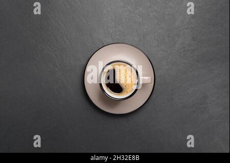 Eine Tasse Kaffee mit schönem Schaum in der Nähe Kaffeebohnen sind auf einem schwarzen Stein Hintergrund Draufsicht Kopierfläche verstreut Stockfoto