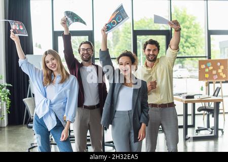 Glückliche, multiethnische Geschäftsleute, die im Büro Dokumente sammeln Stockfoto