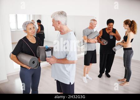 Seniorenpaar mit Übungsmatten unterhalten sich nach dem Yoga-Kurs mit anderen Menschen im Hintergrund Stockfoto