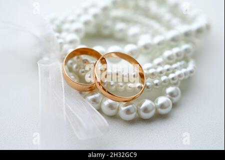 Eheringe und Perlenarmband auf weißem Hintergrund. Brautzubehör aus nächster Nähe. Klassische Hochzeit goldenen Bands. Stockfoto