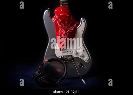 Silberne E-Gitarre mit rotem Bandana isoliert auf schwarzem Hintergrund. Stockfoto