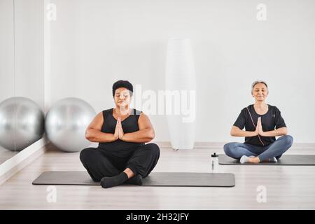 Portrait von zwei älteren Frauen, die sich während des Yoga-Übens mit geschlossenen Augen in Lotusposition entspannen Stockfoto