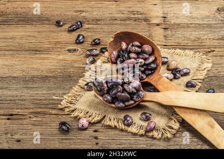 Verschiedene bunte Bohnen in großen Holzlöffeln. Rohe gesunde Zutat für das Kochen von nützlichen Lebensmitteln. Alter Holztisch, Platz zum Kopieren Stockfoto