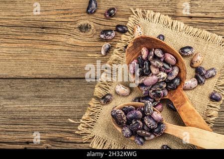 Verschiedene bunte Bohnen in großen Holzlöffeln. Rohe gesunde Zutat für das Kochen von nützlichen Lebensmitteln. Alter Holztisch, Blick von oben Stockfoto