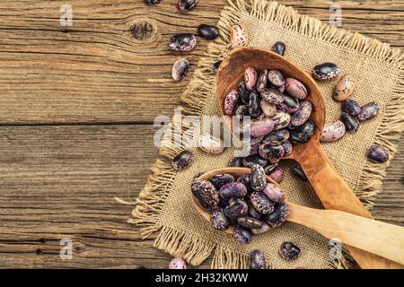 Verschiedene bunte Bohnen in großen Holzlöffeln. Rohe gesunde Zutat für das Kochen von nützlichen Lebensmitteln. Alter Holztisch, Blick von oben Stockfoto