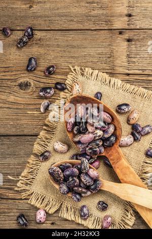 Verschiedene bunte Bohnen in großen Holzlöffeln. Rohe gesunde Zutat für das Kochen von nützlichen Lebensmitteln. Alter Holztisch, Blick von oben Stockfoto