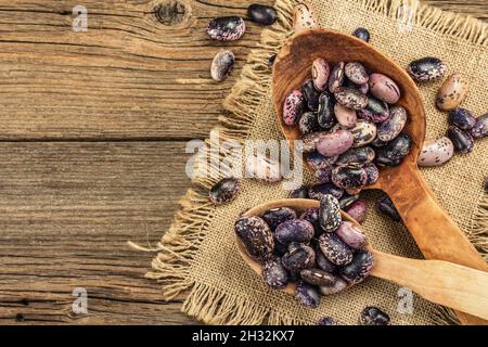 Verschiedene bunte Bohnen in großen Holzlöffeln. Rohe gesunde Zutat für das Kochen von nützlichen Lebensmitteln. Alter Holztisch, Blick von oben Stockfoto
