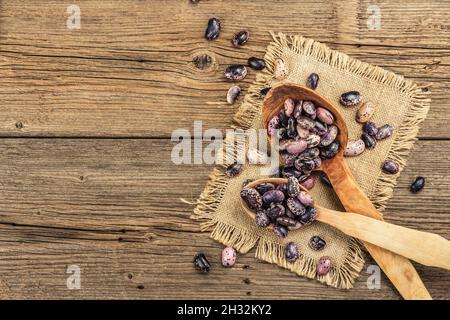 Verschiedene bunte Bohnen in großen Holzlöffeln. Rohe gesunde Zutat für das Kochen von nützlichen Lebensmitteln. Alter Holztisch, Blick von oben Stockfoto