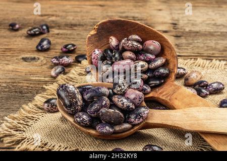 Verschiedene bunte Bohnen in großen Holzlöffeln. Rohe gesunde Zutat für das Kochen von nützlichen Lebensmitteln. Alter Holztisch, Nahaufnahme Stockfoto