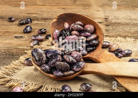Verschiedene bunte Bohnen in großen Holzlöffeln. Rohe gesunde Zutat für das Kochen von nützlichen Lebensmitteln. Alter Holztisch, Nahaufnahme Stockfoto