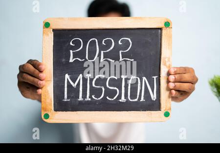 Konzeptvorstellung der Neujahrsmission 2022 - unkenntlich Mann zeigt 2022 Mission schriftliche Schildertafel vom Arbeitsplatz Stockfoto