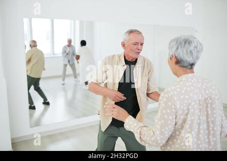 Glückliches Seniorenpaar, das Spaß hat und während des Unterrichts im Tanzstudio mit anderen Leuten tanzt Stockfoto