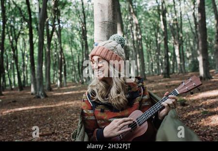 Frau saß glücklich in einer Hängematte und spielte die Ukulele in einem Wald Stockfoto