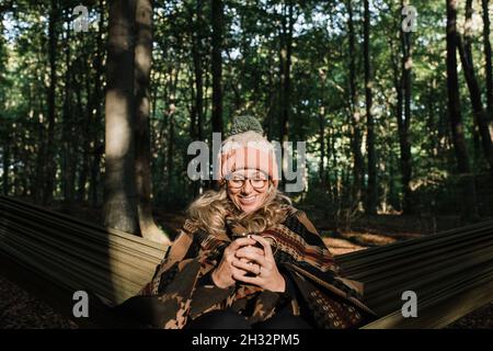 Frau saß glücklich in einer Hängematte im Wald und hatte Kaffee Stockfoto