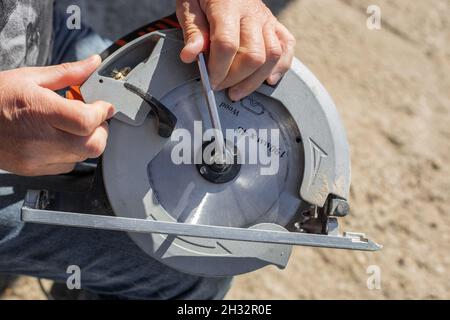 Ein Mann schraubt ein Sägeblatt mit einem Sechseck auf eine Kreissäge für die Holzbearbeitung. Stockfoto