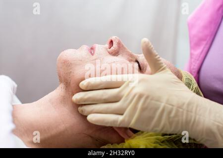 Kosmetikerin reinigt das Gesicht der Frau mit massierenden Bewegungen mit einem Peeling. Stockfoto