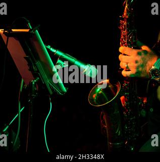 Nahaufnahme der Hände des Künstlermusikers spielt das Saxophon bei einem Konzert vor dem von orangefarbenem Licht beleuchteten Mikrofon Stockfoto