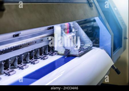 Großer Tintenstrahldrucker, der in der Werkstatt blaue Farbe auf Vinylpapier druckt Stockfoto