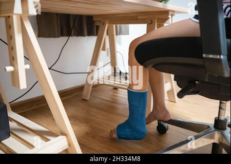 Verletzte Frau mit gebrochenem Bein im Gipsguss, die am Holzschreibtisch arbeitete Stockfoto