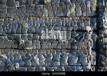 Schwarz verbrannte Wand eines rustikalen Blockhauses an einem hellen Sommer sonnigen Tag. Kohlen. Strukturierte Oberfläche. Nahaufnahme Stockfoto