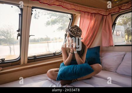 Schöne junge asiatische Frau, die sich abends entspannt und die Aussicht im Wohnheim auf dem Campingplatz ausschaut Stockfoto
