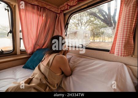 Schöne junge asiatische Frau, die sich abends entspannt und die Aussicht im Wohnheim auf dem Campingplatz ausschaut Stockfoto