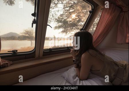 Schöne junge asiatische Frau, die sich abends entspannt und die Aussicht im Wohnheim auf dem Campingplatz ausschaut Stockfoto
