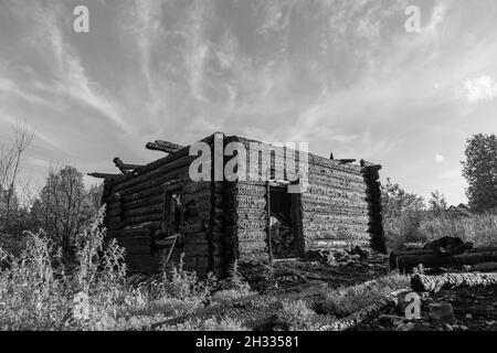 Verbranntes altes Blockhaus in einem Dorf an einem Sommertag gegen einen grauen Himmel. Schwarzweiß-Bild. Nahaufnahme Stockfoto