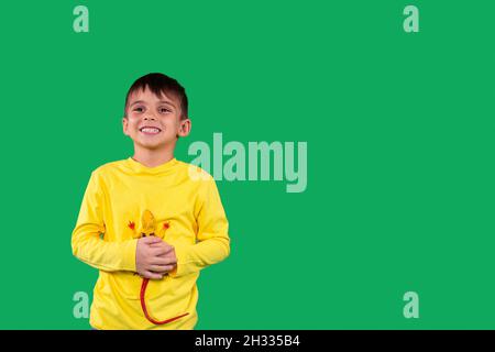 Fröhliches Kind mit gelbem Hoodie und lächelndem Gesichtsausdruck, das das Dinosaurier-Spielzeug in den Händen hält, Raum kopieren. Stockfoto