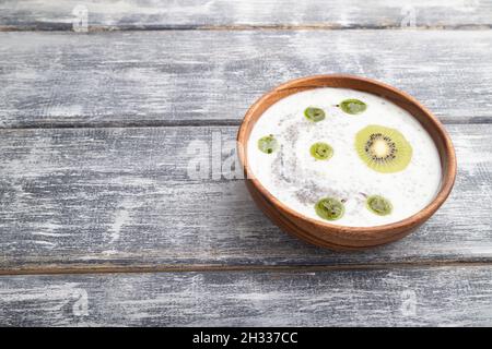 Joghurt mit Kiwi, Stachelbeere, Chia und Mandeln in Holzschüssel auf grauem Holzhintergrund. Seitenansicht, Kopierraum, Nahaufnahme. Stockfoto